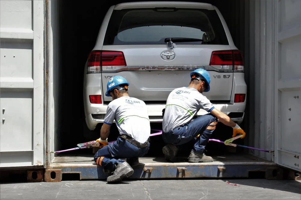 Workers securing a vehicle inside a shipping container